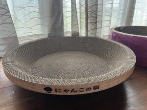 届いた日の新品。木目のふちに「にゃんこの宿」のロゴ。右奥に紫の先代